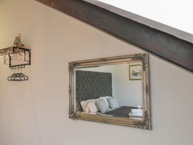 A wall-mounted shelf with hangers and fairy lights next to a large framed mirror reflecting a bed and a painting at Foxton Penthouse in Whitby