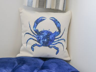 A cushion with a blue crab design placed on a blue upholstered seat at Foxton Penthouse in Whitby