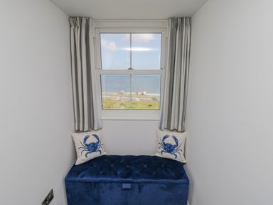 A window with striped curtains over a blue cushioned bench with crab printed pillows at Foxton Penthouse in Whitby