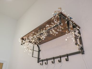 A wooden wall shelf with metal brackets decorated with string lights and hooks underneath at Foxton Penthouse in Whitby