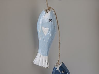 Two wooden fish painted in blue and white hanging on a string against a grey background