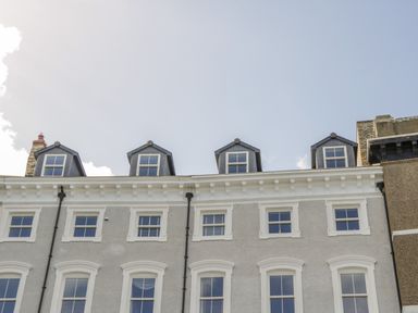 The upper floors of a gray and white building with multiple windows and dormer windows under a clear sky at Foxton Penthouse in Whitby