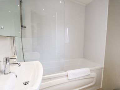 A bathroom with a white sink with faucet and a bathtub with a glass shower screen and towel at Number 10 in Warton