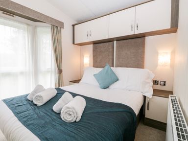 A bedroom with a double bed with white bedding and a teal throw with rolled white towels at Number 10 in Warton