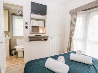 A bedroom with a bed and rolled towels near a window with curtains and an ensuite bathroom at Number 10 in Warton
