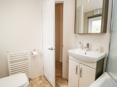 A bathroom with a white toilet towel rack a sink with cabinet and mirror and a partially open door at Number 10 in Warton