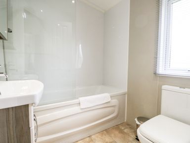 A bathroom with a bathtub shower combination sink and toilet near a window with blinds at Number 10 in Warton