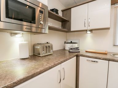 A kitchen countertop with a microwave oven above a paper towel holder and toaster along with shelves and upper cabinets at Number 10 in Warton
