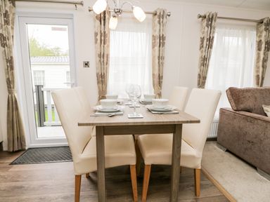 A dining table with four beige chairs set with plates bowls and glasses next to windows with curtains at Number 10 in Warton