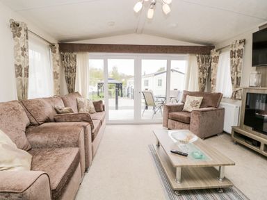 A living room with a brown sofa and armchair a wooden coffee table and large glass doors at Number 10 in Warton