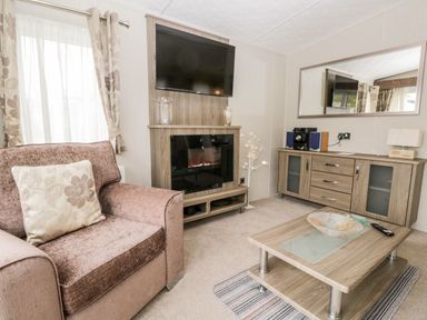 A living room with an armchair a TV mounted over an electric fireplace a sideboard with a stereo and a coffee table at Number 10 in Warton