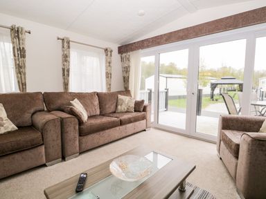 A living room with brown sofas and a coffee table facing sliding glass doors at Number 10 in Warton