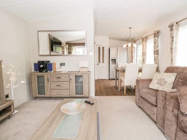 A living room with a sofa a coffee table and a sideboard and a dining area with chairs and a table and a refrigerator at Number 10 in Warton