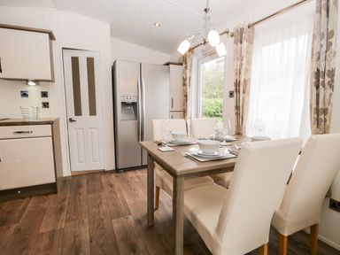 A dining area with a wooden table set with plates bowls glasses and cutlery surrounded by white chairs next to a kitchen with modern cabinets and a stainless steel refrigerator at Number 10 in Warton