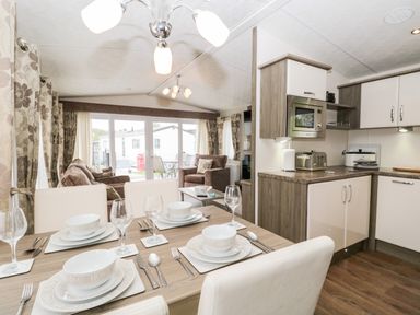 A dining table set with plates and glasses next to a kitchen area with cabinets and appliances at Number 10 in Warton