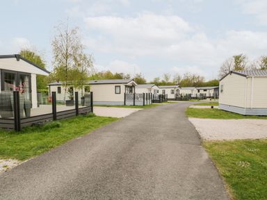 A paved road with mobile homes on both sides and grass areas at Number 10 in Warton