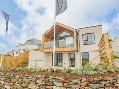A modern two-story house with wood and glass balcony and stone retaining wall at Porth Beach in Porth near St Columb Minor