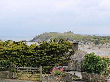 A seaside view with a rocky hill grassy landscape wooden fence and a house at Porth Beach in Porth near St Columb Minor