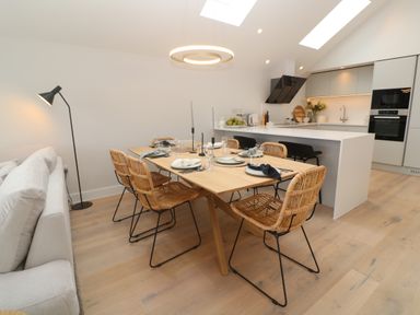 A dining area with a wooden table set for six and a kitchen with white cabinets and appliances at Porth Beach in Porth near St Columb Minor