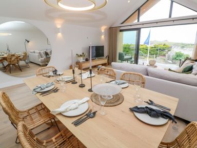 A dining table set with plates, cutlery, and candles in a room with a sofa and large window showing an outdoor view at Porth Beach in Porth near St Columb Minor