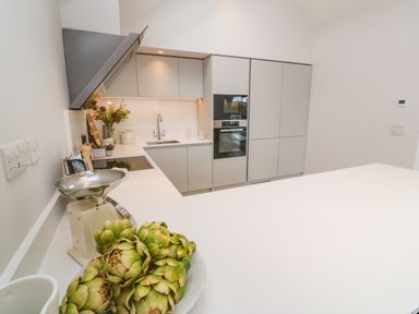 A modern kitchen with white countertops cabinets sink oven and green artichokes on the counter at Porth Beach in Porth near St Columb Minor