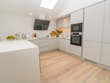 A kitchen with white cabinets wooden floor built in oven and microwave and a black cooker hood at Porth Beach in Porth near St Columb Minor