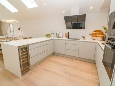 A modern kitchen with white countertops light wood flooring a wine cooler and built in oven at Porth Beach in Porth near St Columb Minor