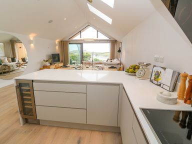 A modern kitchen with white countertops and cabinets overlooking a dining area and living room at Porth Beach in Porth near St Columb Minor