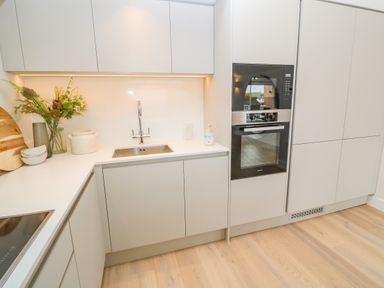 A kitchen with white cabinets a sink an oven a microwave and flowers on the counter at Porth Beach in Porth near St Columb Minor