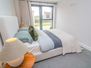 A bedroom with a double bed beside a wooden side table with a lamp and glass door at Porth Beach in Porth near St Columb Minor