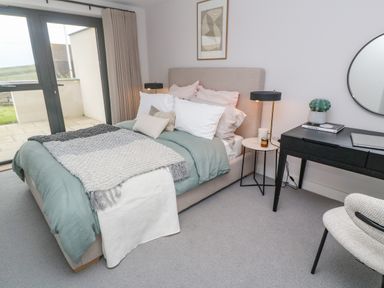 A bedroom with a bed bedside tables lamps a desk chair and a round mirror at Porth Beach in Porth near St Columb Minor