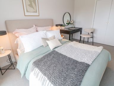 A bedroom with a bed with pillows and a blanket a side table with a lamp a desk with a mirror and chair at Porth Beach in Porth near St Columb Minor