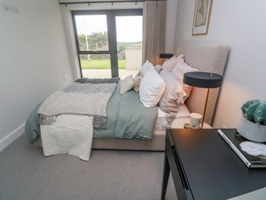 A bedroom with a bed near glass doors and a black table with a lamp and books at Porth Beach in Porth near St Columb Minor