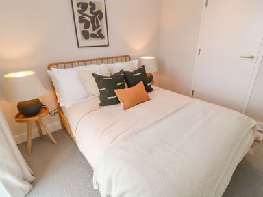 A bedroom with a wooden bed frame white bedding pillows bedside tables with lamps and abstract artwork on the wall at Porth Beach Porth near St Columb Minor