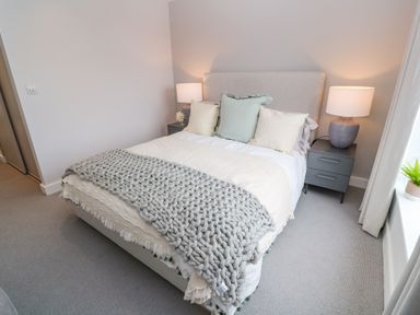 A bedroom with a bed with pillows and a knitted blanket with two bedside tables with lamps by a window at Porth Beach in Porth near St Columb Minor