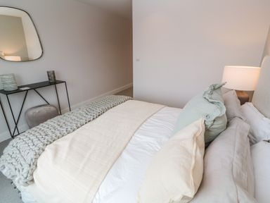 A bedroom with a bed with pillows and blankets a lamp on a nightstand a black metal console table with decorative items and a mirror on the wall at Porth Beach in Porth near St Columb Minor