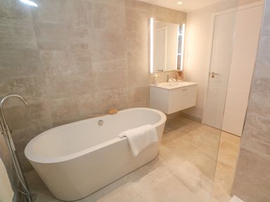 A bathroom with a freestanding bathtub a towel on the tub a sink with a mirror and a door at Porth Beach in Porth near St Columb Minor