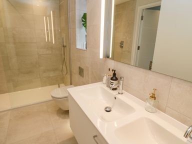 A bathroom with a double sink vanity a wall-mounted toilet and a glass-enclosed shower at Porth Beach in Porth near St Columb Minor