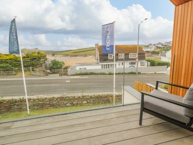 A balcony with a chair overlooking a road with houses and a beach in the background at Porth Beach in Porth near St Columb Minor