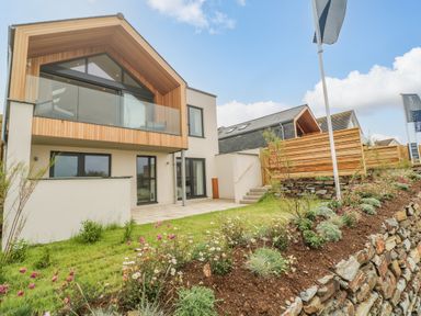 Exterior of a modern two-story house with a wooden balcony and garden at Porth Beach in Porth near St Columb Minor