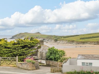 A coastal scene with houses trees a sandy beach and a grassy hill at Porth Beach in Porth near St Columb Minor