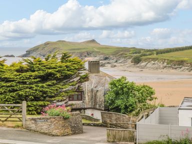 A coastal view with a house in front of a beach and a grassy headland at Porth Beach in Porth near St Columb Minor