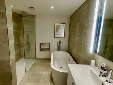 A bathroom with a freestanding bathtub a walk-in shower a sink with soap dispenser and a wall mirror at Porth Beach in Porth near St Columb Minor