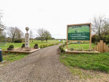 Entrance to a golf course with a gravel path and a welcome sign at Freddy's Lodge Foxburrow Hang in Fritton
