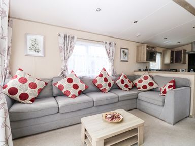 A living room with a gray sectional sofa with red and white patterned cushions a wooden coffee table and framed pictures on the wall at Freddy's Lodge Foxburrow Hang in Fritton