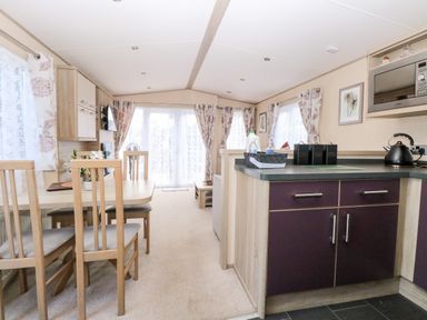 A dining area with wooden chairs and a table next to a kitchen with dark cabinets and a microwave at Freddy's Lodge Foxburrow Hang in Fritton