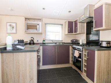 A kitchen with purple cabinets a microwave kettle stove and window at Freddys Lodge Foxburrow Hang in Fritton