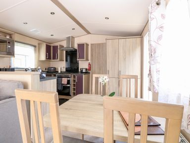 A kitchen and dining area with wooden cabinets and chairs and a small flower on the table at Freddy's Lodge Foxburrow Hang in Fritton