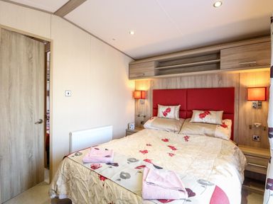 A bedroom with a bed with floral bedding towels on the bed bedside tables and wall shelves at Freddy's Lodge Foxburrow Hang in Fritton