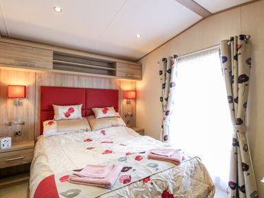 A bedroom with a double bed red headboard floral bedding bedside shelves and curtains at Freddy's Lodge Foxburrow Hang in Fritton